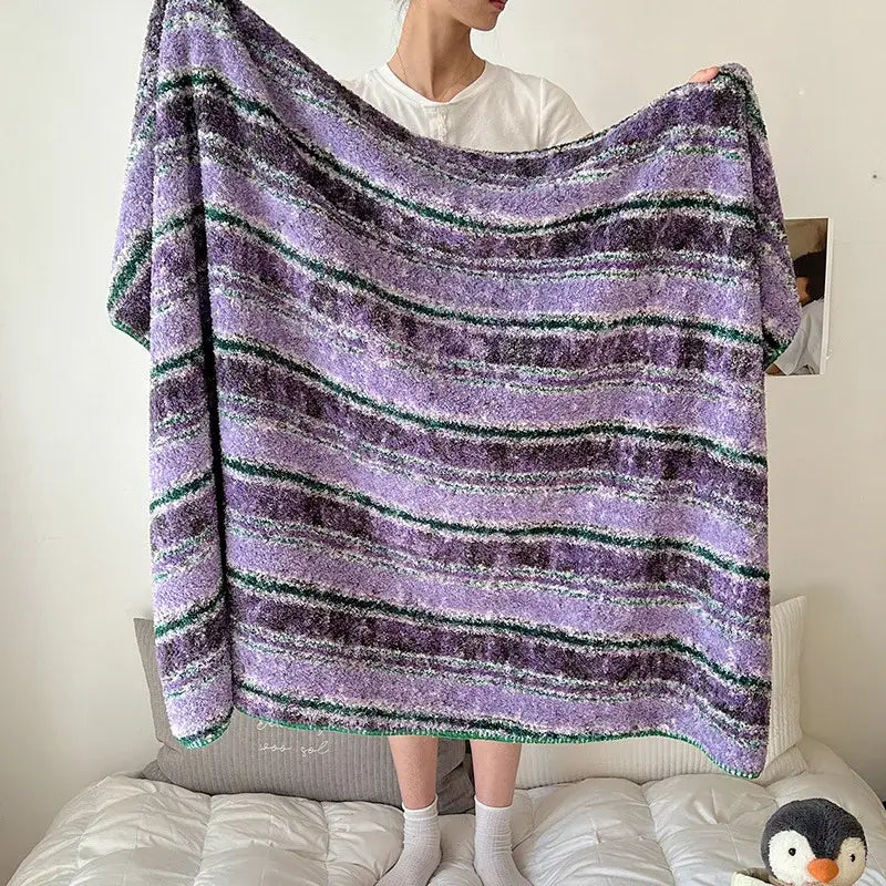 A plush boho printed blanket with fuzzy horizontal stripes in purples and dark green for cozy bedroom use
