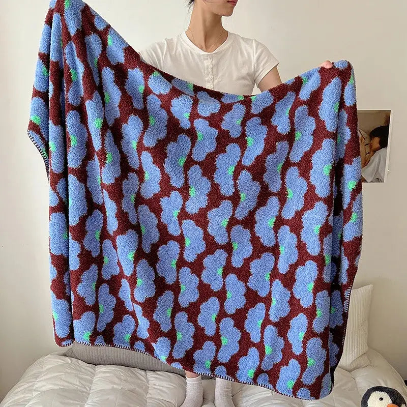 A plush boho printed blanket with light blue cloud patterns and green accents on a maroon chunky knit shawl