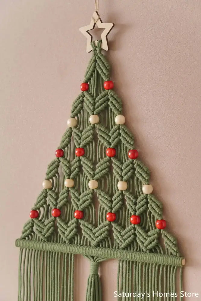 A sage green and cream macrame christmas tree wall hanging with red and cream beads and wooden star decorbites boho christmas