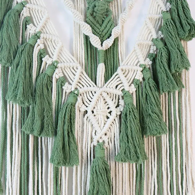 Boho sage green and white wall hanging featuring an intricate macrame tassel stick with symmetrical cords and diamond pattern