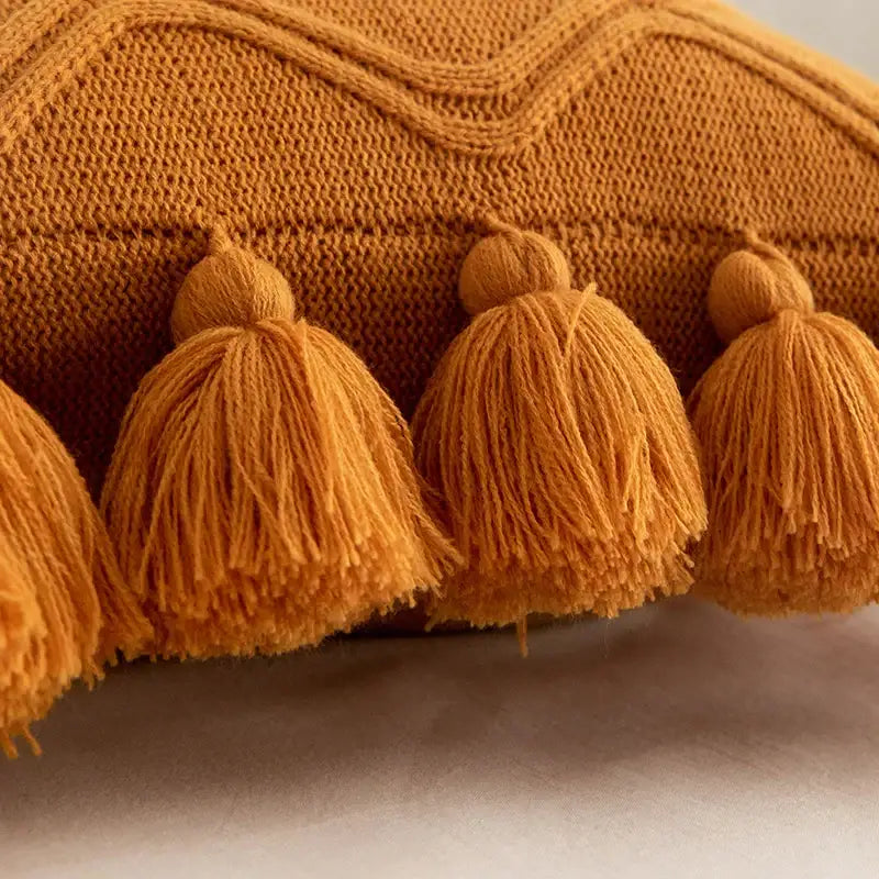 Warm amber-colored knit cushion cover with a textured wavy pattern and tassels from decorbites boho style ivory collection