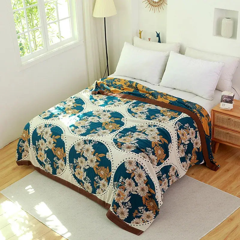 A cozy boho teal floral cotton cover throw blanket with gold pattern and brown border draped on a bed