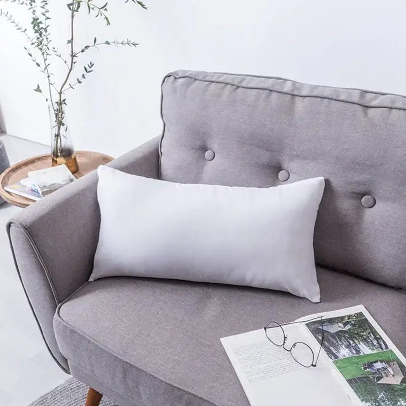 A sleek white rectangular pillow with smooth fabric on a gray sofa featuring decorbites boho tufted embroidered cushion cover