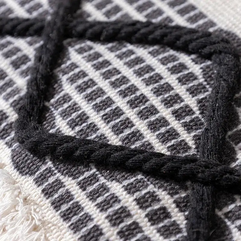 Black braided rope detail woven over textured white and gray checkered fabric on boho tufted fringed black pillowcase decorbites