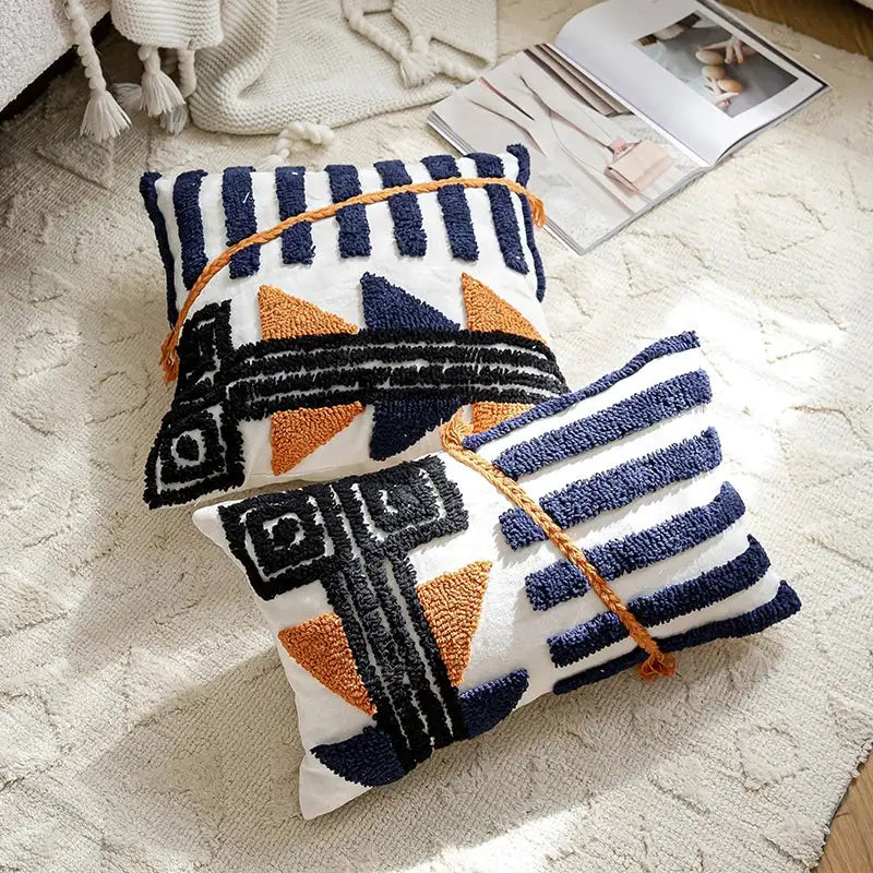 Two rectangular decorbites boho tufted pillow covers with navy and burnt orange geometric patterns tied with braided cord