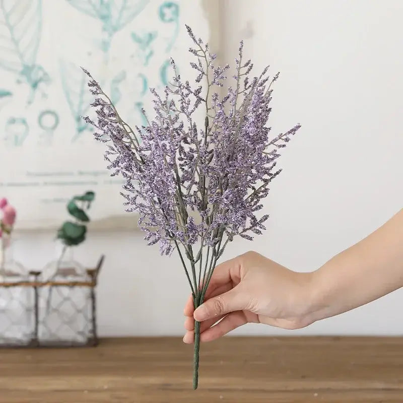 A hand holding a delicate lavender artificial flower bouquet with slender stems featuring decorbites forever dancing grass