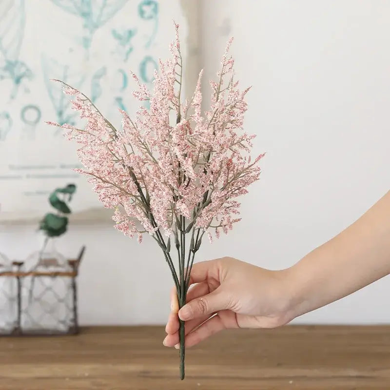 A delicate bouquet of artificial pink baby’s breath flowers with forever dancing grass held in a boho wicker basket