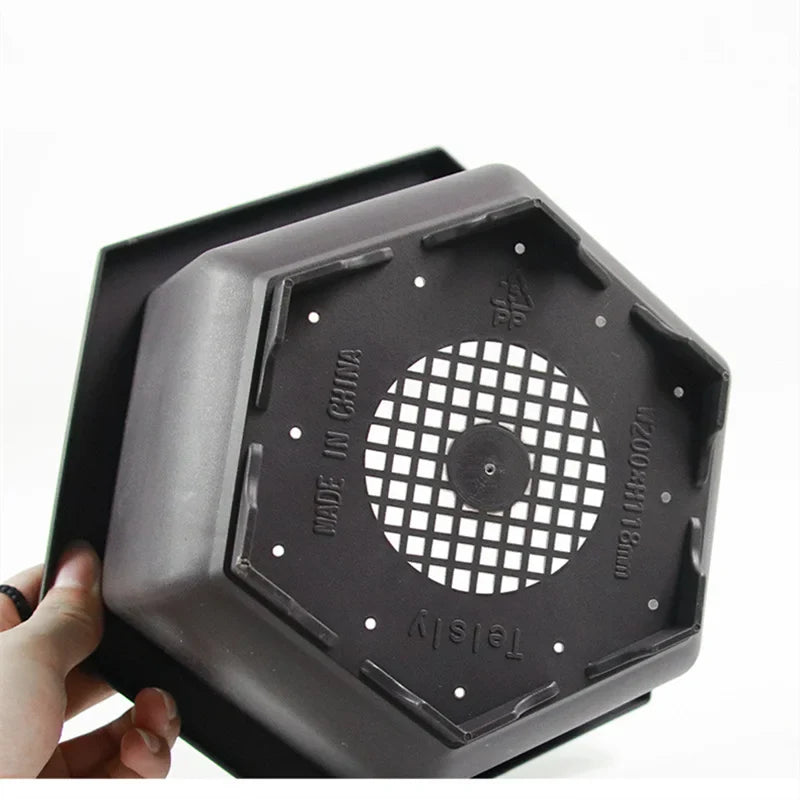Black hexagonal plastic plant pot with grid-patterned drainage hole and molded edges for outdoor garden use para plantas