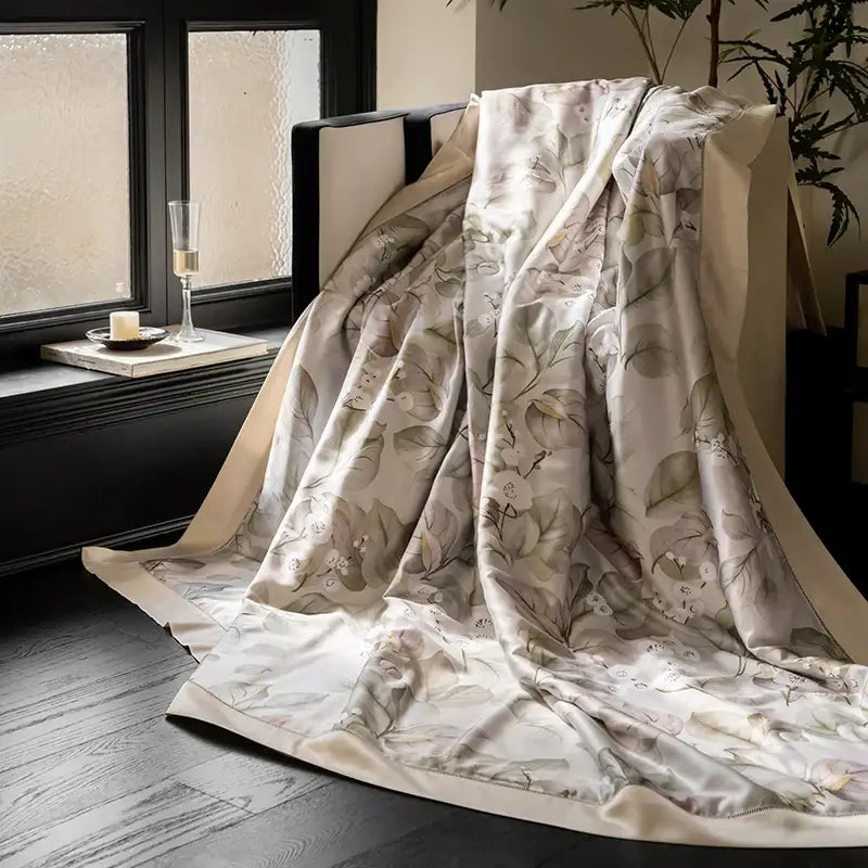 A cream silk throw blanket with botanical eucalyptus fiber flowers print draped over a dark chair for quilt set decorbites