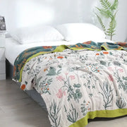 A soft off-white decorbites cotton leisure blanket with delicate pink and green botanical print and lime-green border