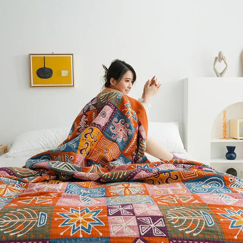 A cozy botanical orange and blue cotton gauze blanket bedspread draped over a person with decorbites birds plaid pattern