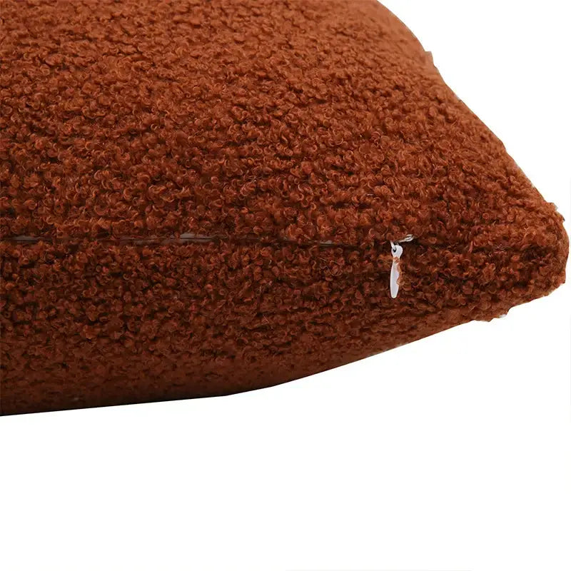 A cozy rust-colored boucle teddy throw pillow with plush curly texture and a small silver zipper pull for living room decor