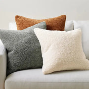Three plush boucle teddy throw pillows in rust orange slate gray and cream arranged on a light sofa for decorbites decor