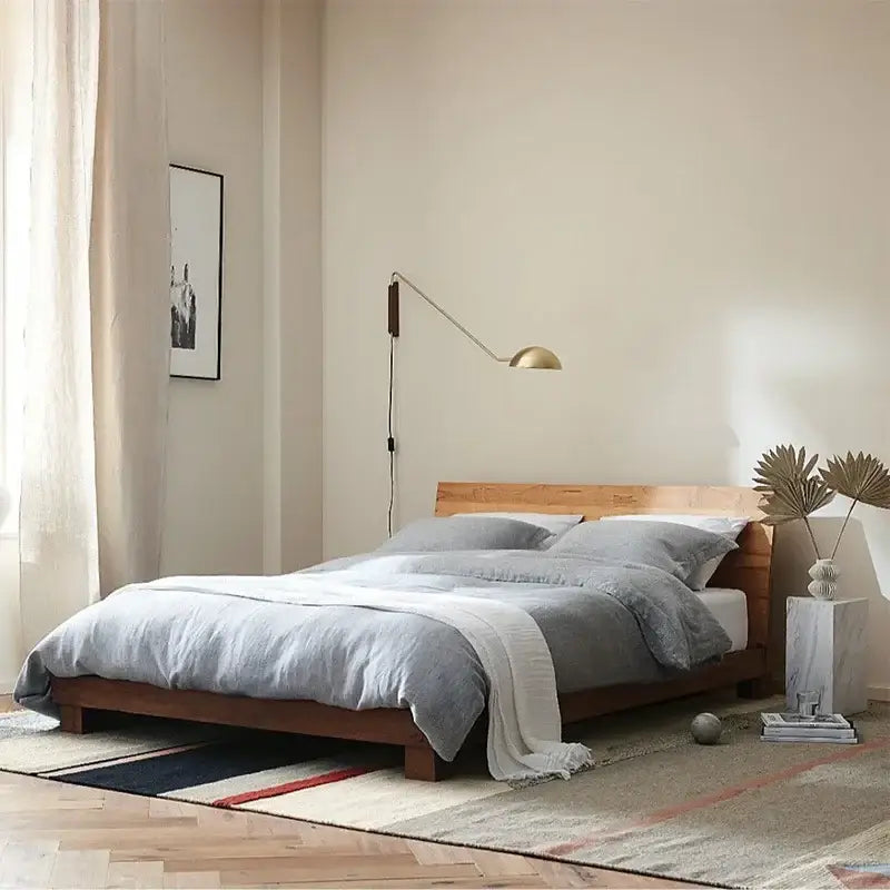 A minimalist wooden bed with gray linen bedding illuminated by a brass and wood adjustable metal wood wall lamp