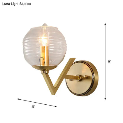 Brass ball sconce with gold-toned ribbed glass shade and exposed filament bulb for bedroom wall lighting