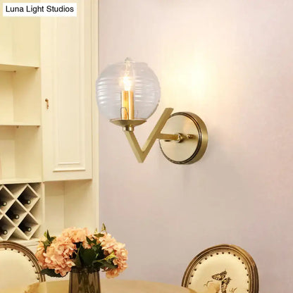 Brass ball sconce with ribbed glass shade and exposed filament bulb for bedroom wall lighting in gold tone