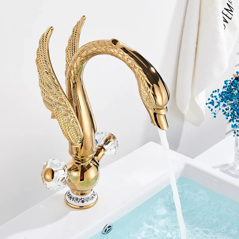 Brass basin faucet deck mounted in antique brass featuring a golden swan shape with ornate feathered wings and crystal knobs