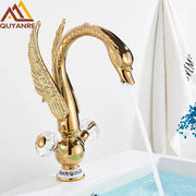 Brass basin faucet deck mounted shaped like a golden swan with intricate feather detailing and crystal knobs in antique brass