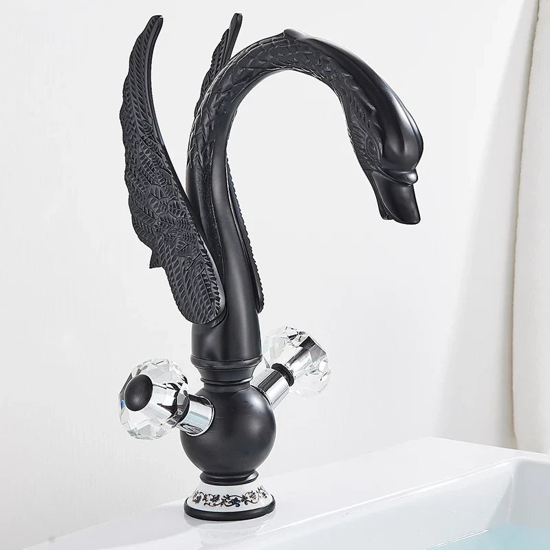 Brass basin faucet deck mounted with black swan design, antique brass finish, crystal knobs, and ornate wing detailing