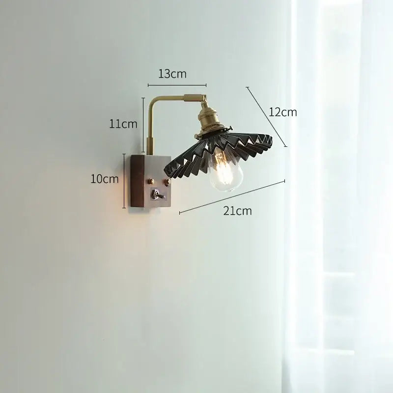 Industrial-style led wall light with brass ceramic arm and black fan-shaped shade cradling an exposed bulb for living room
