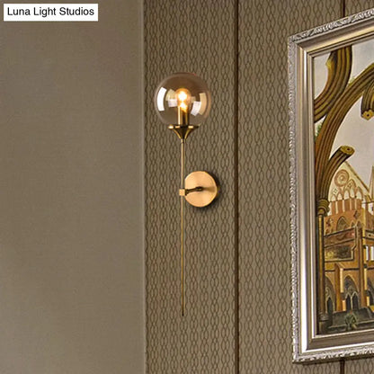Aplique de pared con pantalla esférica de latón - Luz moderna de un solo foco con cristal transparente/gris/ámbar para dormitorio