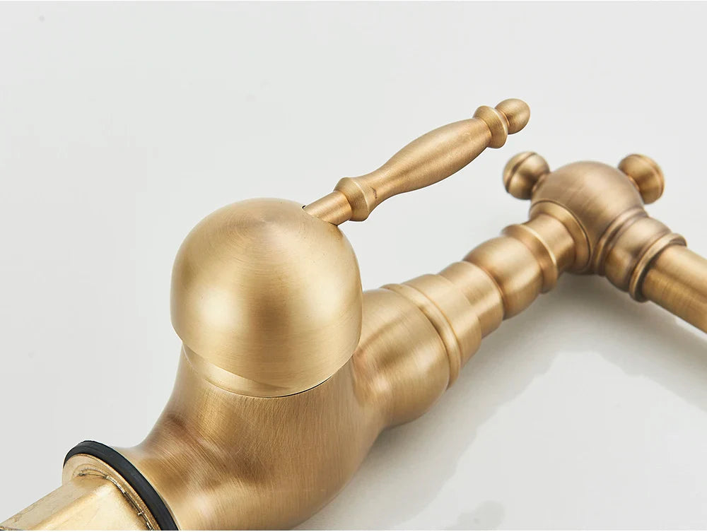 Antique brass finished deck mounted kitchen faucet with rotating neck, spherical spout, and ornate turned wood-style handles