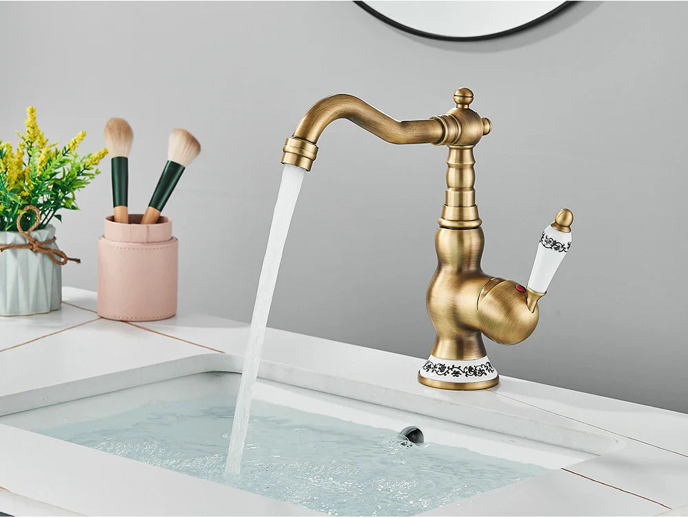 Antique brass deck mounted kitchen faucet with ornate detailing white ceramic handles and rotating neck mechanism