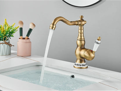 Antique brass deck mounted kitchen faucet with ornate detailing white ceramic handles and rotating neck mechanism