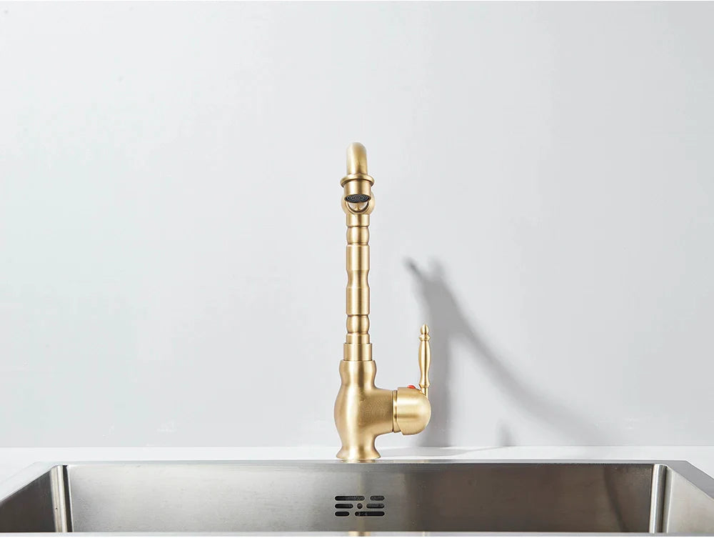 Brass kitchen faucet deck mounted with a rotating tall segmented spout and ornate handle design in brass finish