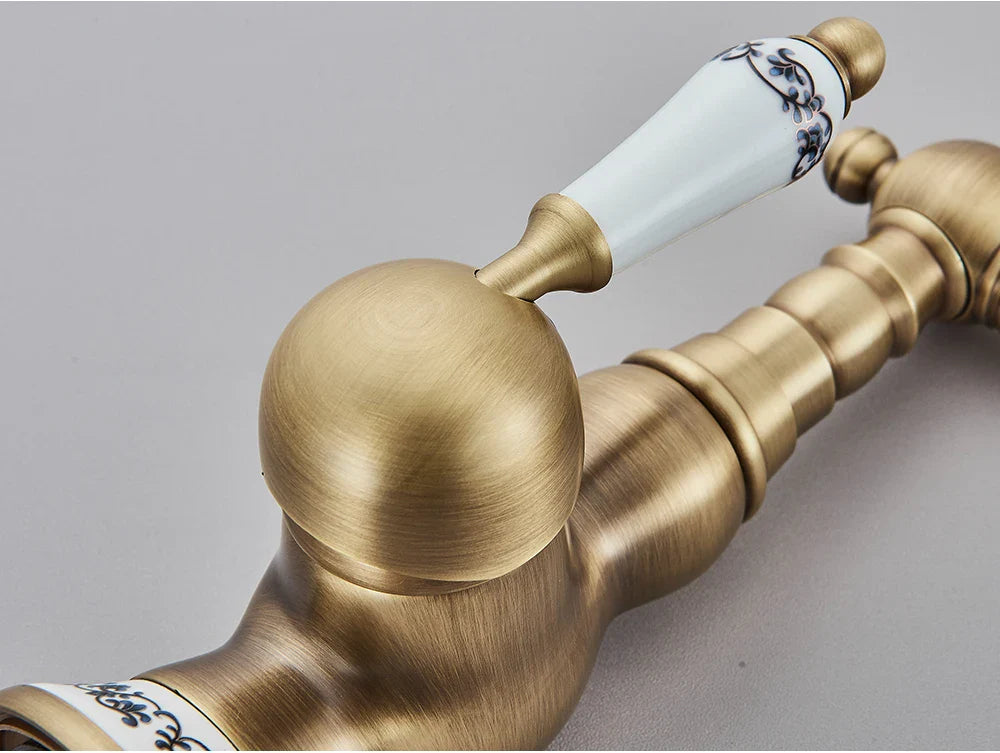 Antique brass kitchen faucet with rotating neck and deck mounted design featuring white ceramic handle with blue floral patterns