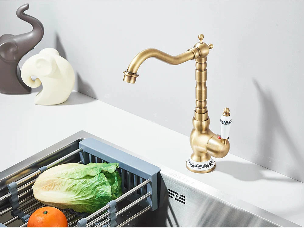Antique brass deck mounted kitchen faucet with rotating neck, ornate fluted spout, and ceramic decorative handles