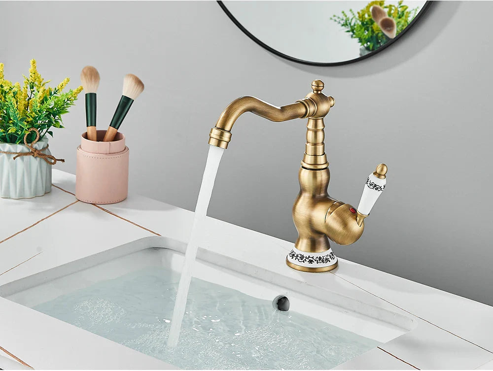 Antique brass deck mounted kitchen faucet with rotating neck and white ceramic handle featuring black floral patterns