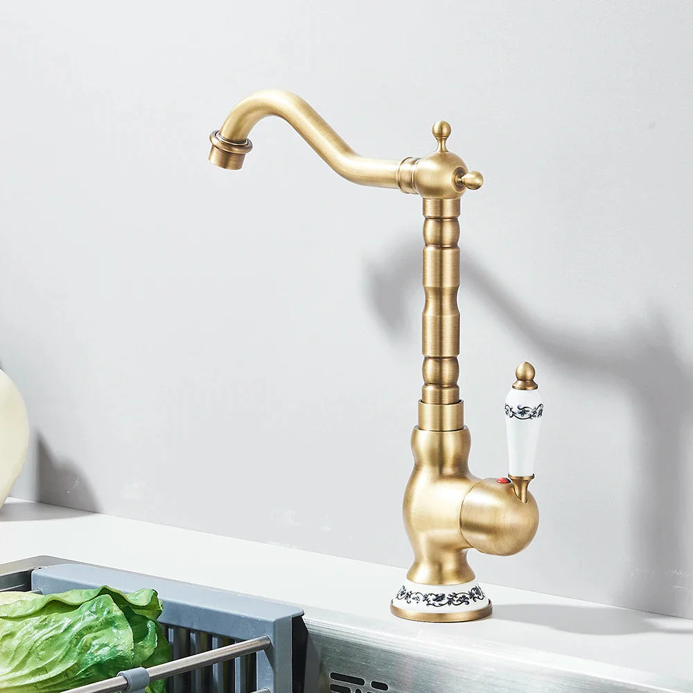 Antique brass deck mounted kitchen faucet with a rotating neck curved spout and decorative ceramic handle