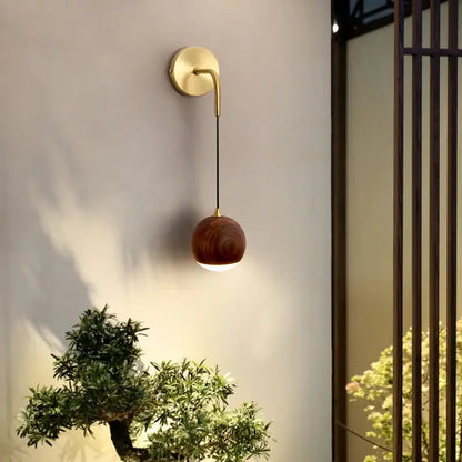 A sleek brass wall lamp with led walnut wood spherical shade by decorbites emitting soft ambient light
