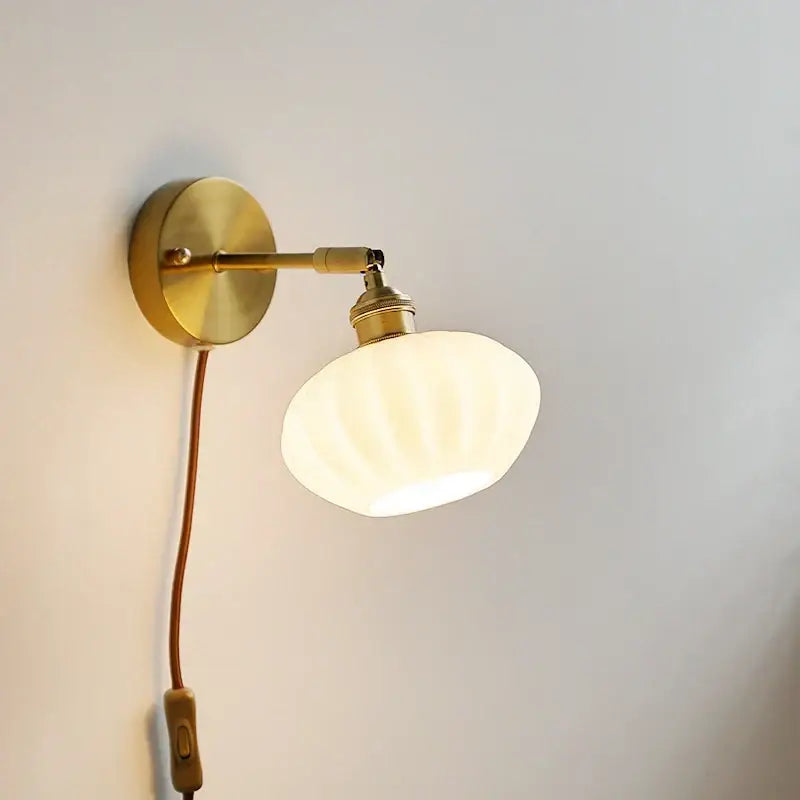A warm brass decorbites ceramic led wall sconce with ribbed off-white glass shade for bedroom mirror lighting