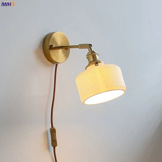 Brass ribbed decorbites ceramic wall sconce with iron arm, off-white ribbed ceramic shade, and brown cord for bedroom lighting