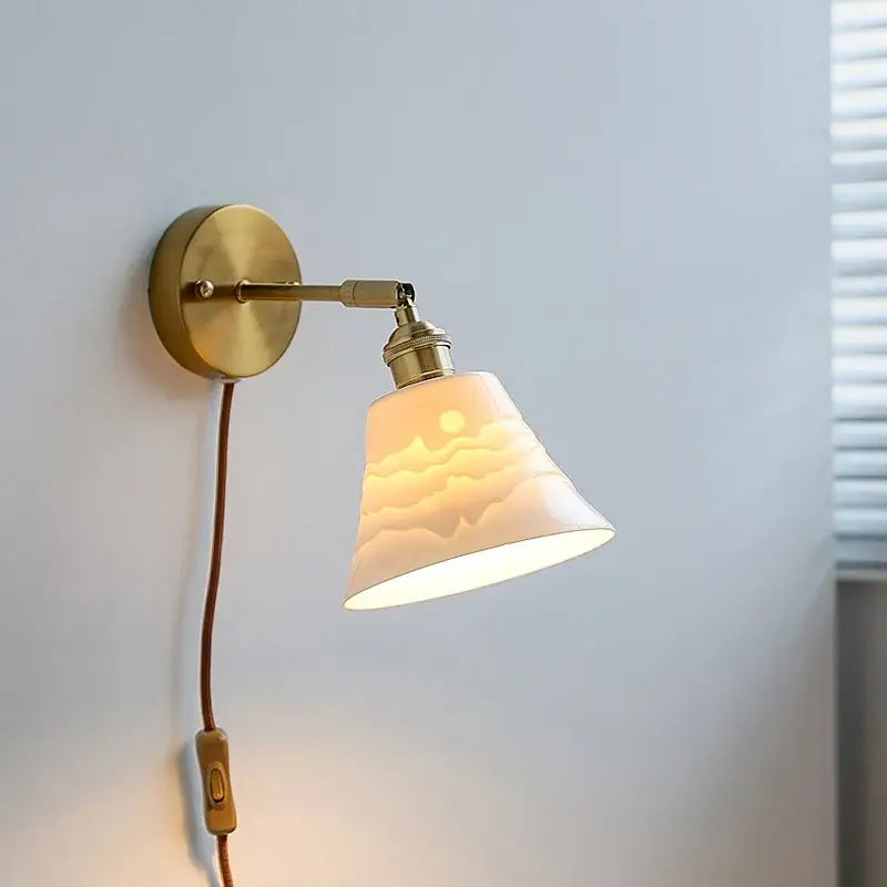 A warm-toned brass wall sconce with an iron arm and decorbites ceramic shade featuring a sunrise design