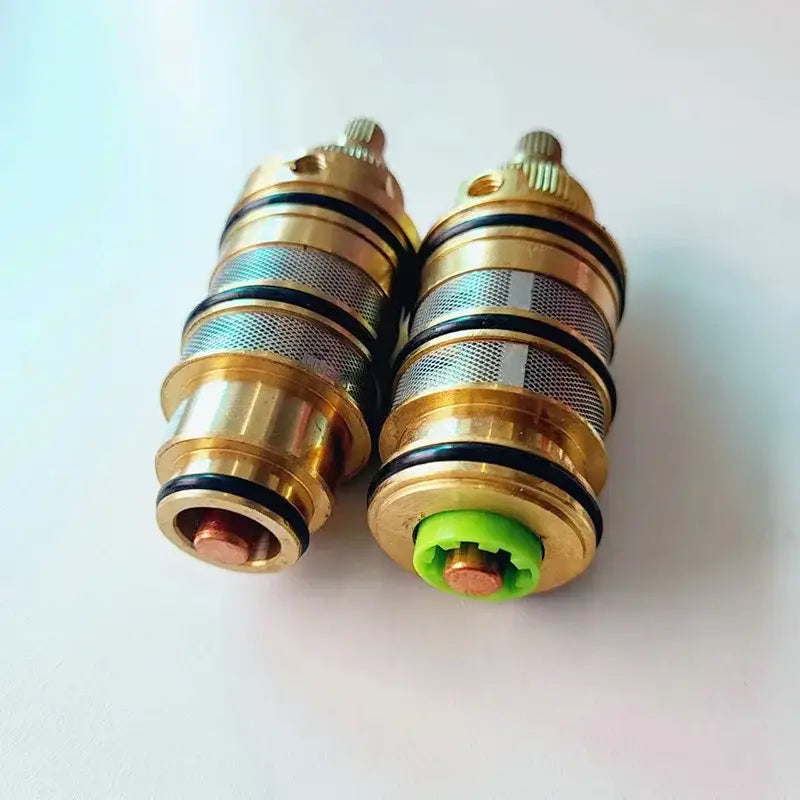 Two brass thermostatic mixer cartridges with mesh filters and black seals one with a green decorbites brass thermostatic base component
