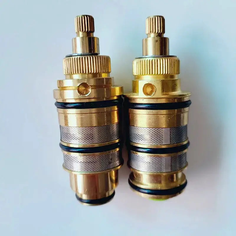 Two brass decorbites thermostatic mixer cartridges with textured ridged tops and silver mesh sections for kitchen use