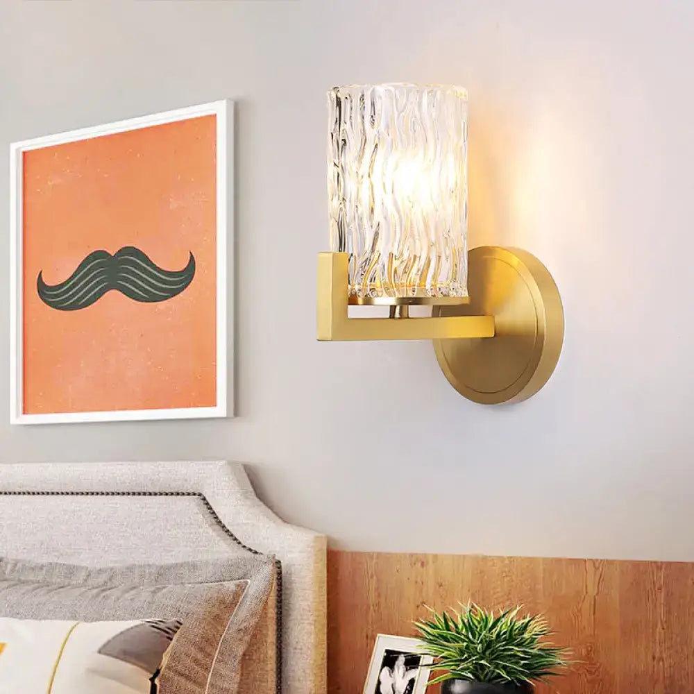 Gold-toned brass wall light with cylinder rippled glass textured clear glass cylinder bedroom sconce
