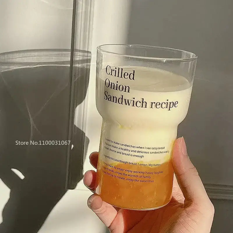 Clear glass coffee mug with black grilled onion sandwich recipe text filled halfway with orange liquid and straw