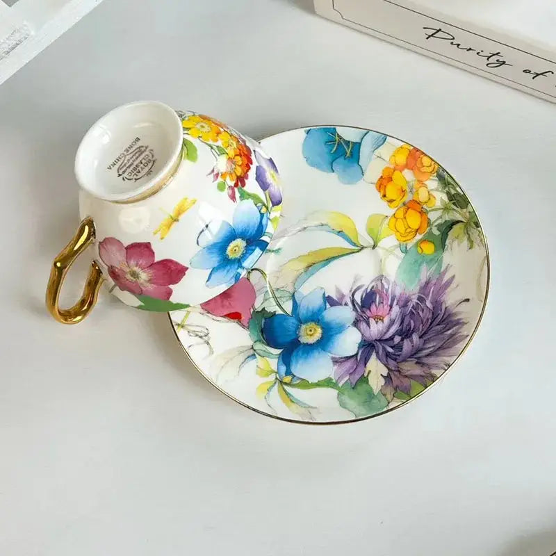 A delicate porcelain teacup and saucer with a brilliant flowers pattern in vibrant colors and gold accents for dining use