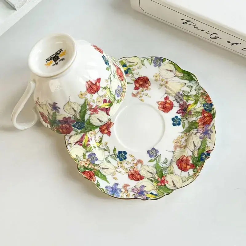 A delicate porcelain teacup and saucer set featuring a brilliant flowers pattern in red blue purple and green hues