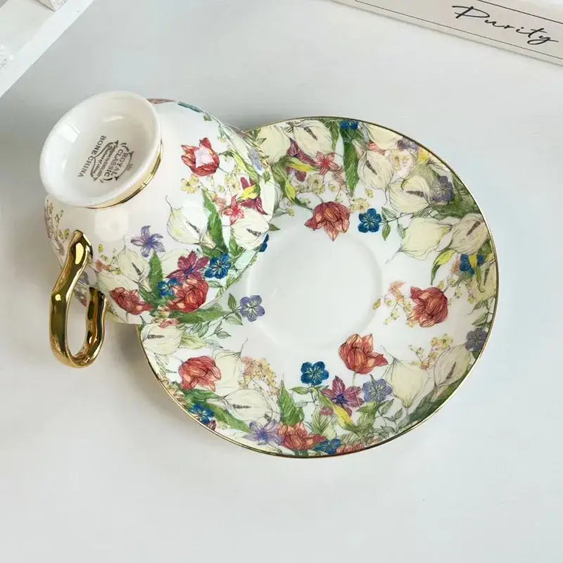 Delicate white porcelain teacup and saucer with a brilliant flowers pattern of red tulips and blue flowers with gold trim