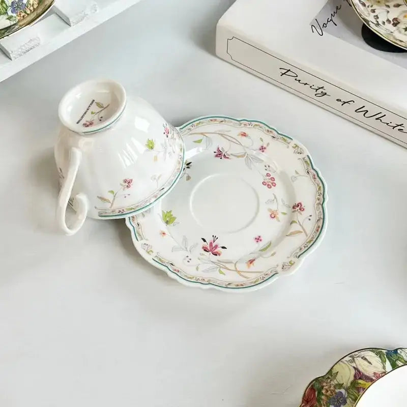 A delicate white porcelain teacup and saucer set with a brilliant flowers pattern in soft pink green and brown hues
