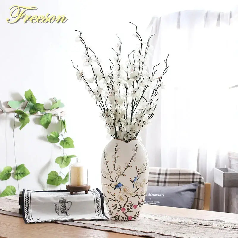 Cream-colored bird butterfly porcelain vase with blue pink floral patterns holding white artificial blossoms for decorbites decor