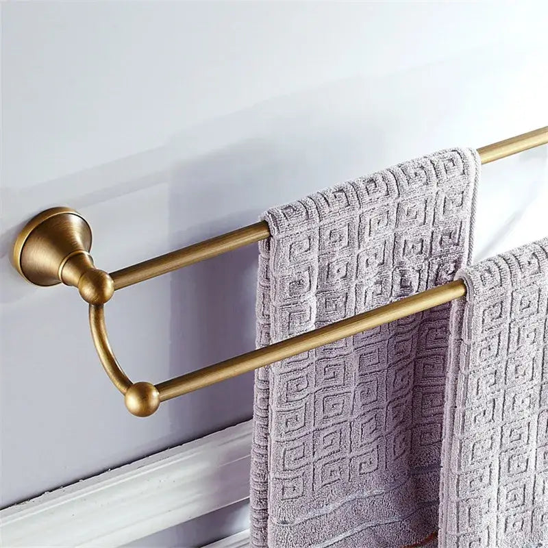 Brass double towel rack with ornate spherical accents holding textured gray towels in decorbites bronze bathroom accessories set