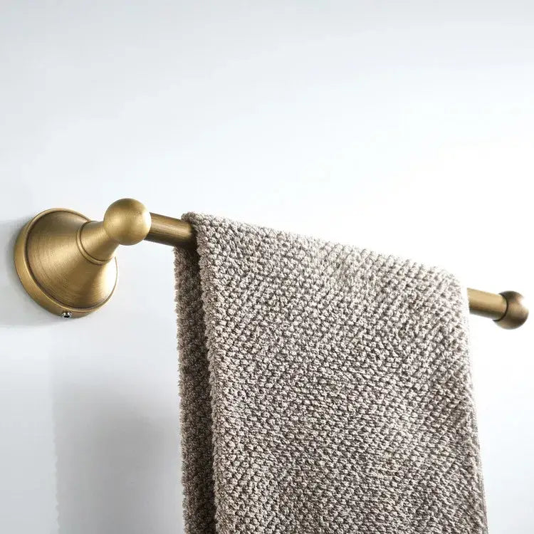 A gray textured towel hangs on an antique brass towel rack featuring ornate spherical finials in a bronze bathroom accessories set