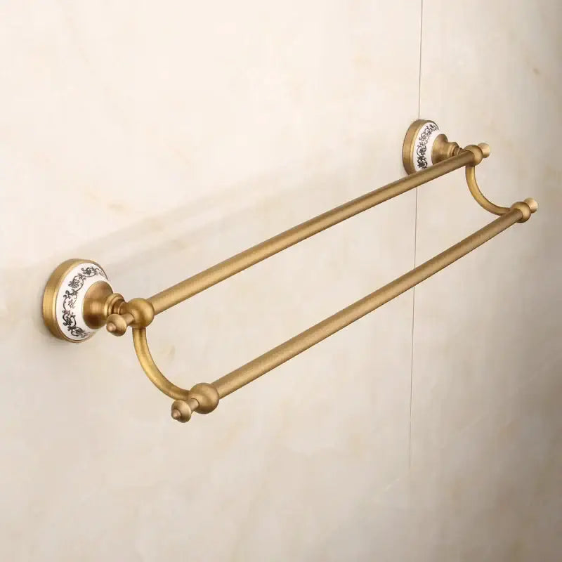 Antique brass double towel rack with ornate white ceramic end caps and black floral detailing in bronze bathroom hardware set