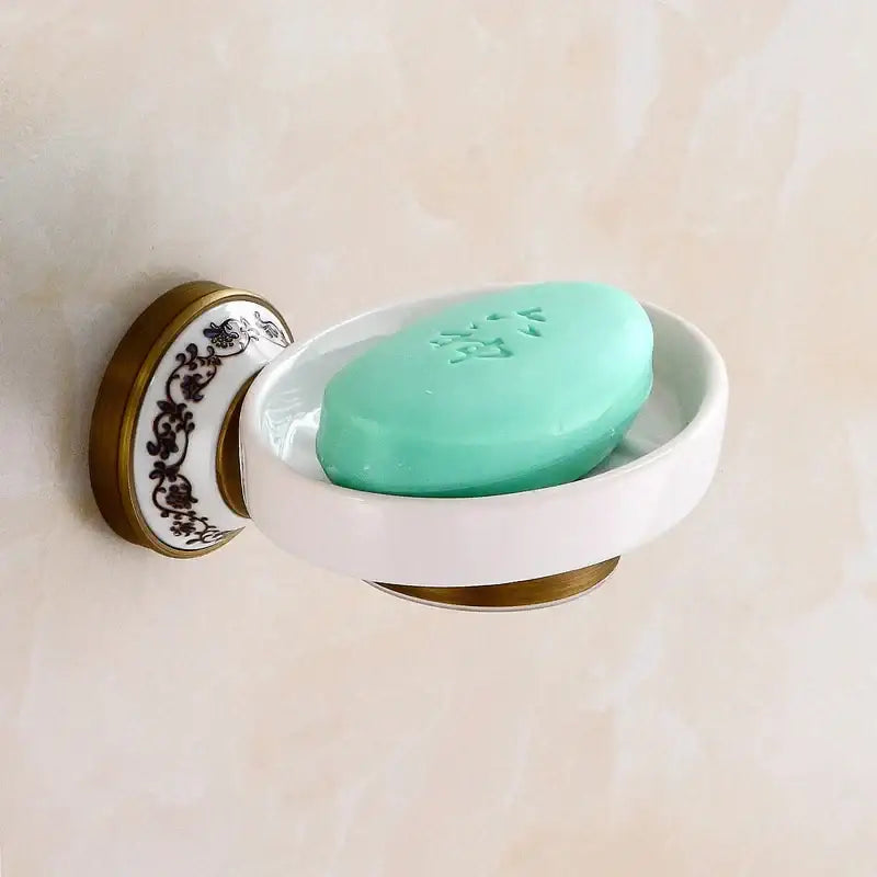 White ceramic soap dish with black floral pattern and gold-toned metal bracket in decorbites bronze bathroom hardware set